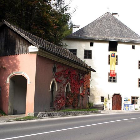 Zwei Gebäude mit unterschiedlichen Architekturstilen, eines mit einer roten Rebe und das andere mit einer Fahne, an einer Straße gelegen.