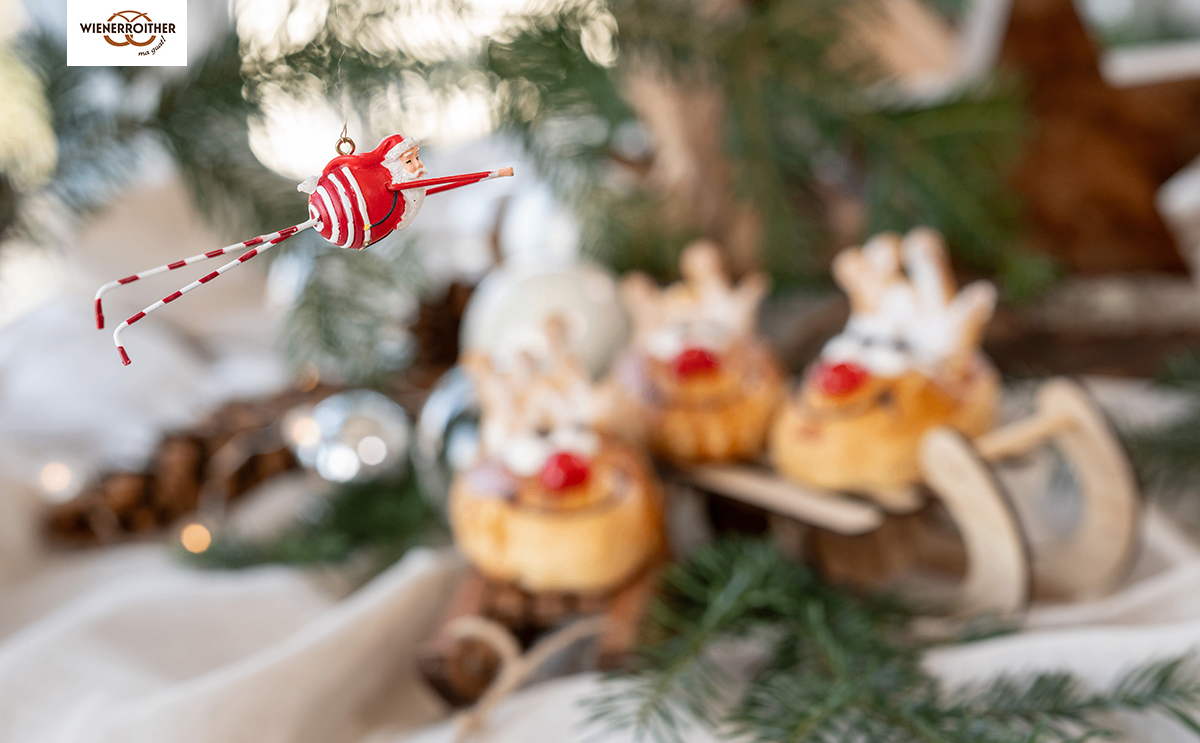 Ein Weihnachtsbaum mit einem Weihnachtsmann-Ornament und Rentier-thematischen Gebäck, umgeben von Tannennadeln und einem verschwommenen Hintergrund.