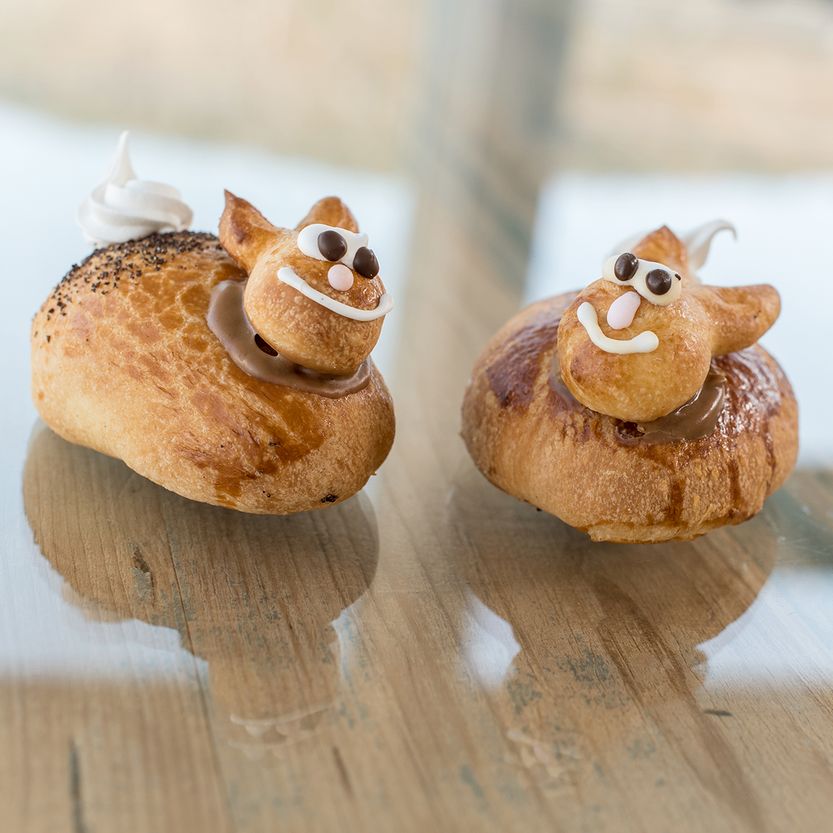 Zwei Gebäckhunde mit Schokolade und Sahne auf einem Holztisch. Jeder hat ein verspieltes Gesicht mit Augen, Nase und Mund.