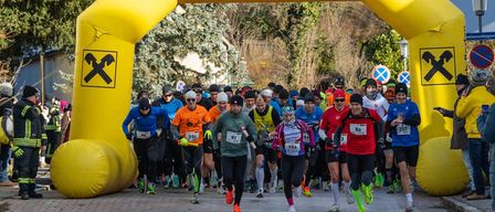 Marathonläufer in warmer Kleidung passieren einen gelben Bogen mit der Aufschrift 'Raiffeisenbank Baden'. Bäume und Schilder sind im Hintergrund zu sehen.