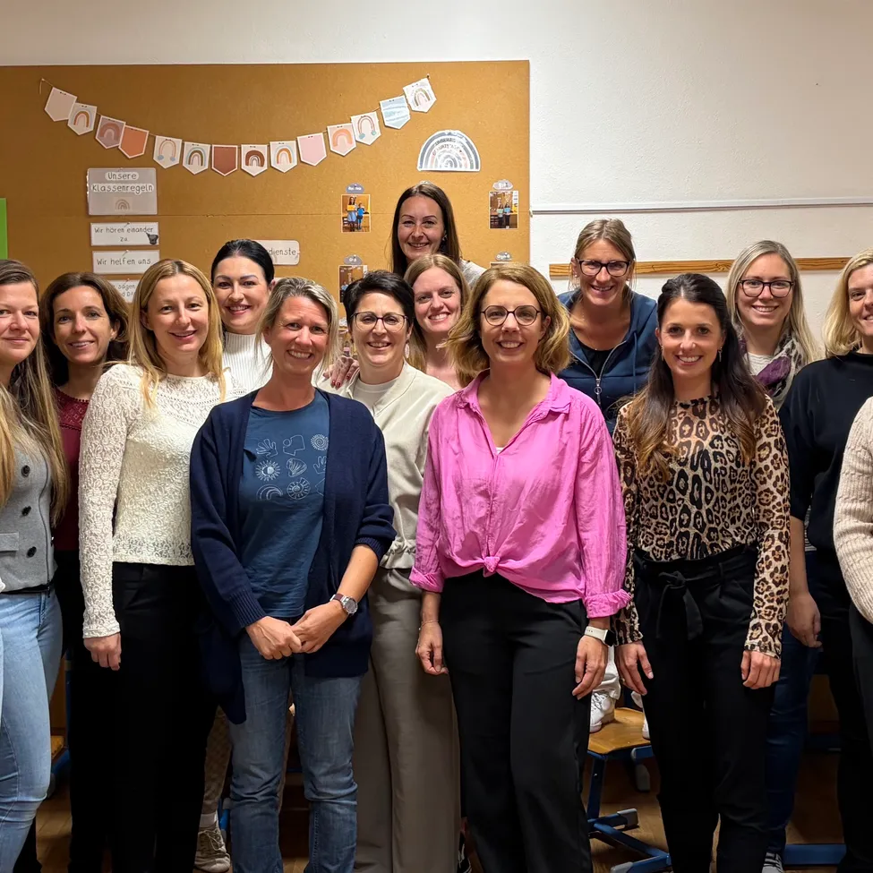 Eine Gruppe von Frauen in einem Klassenzimmer, lächelnd und für ein Foto posierend.
