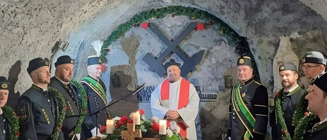 Ein Priester leitet eine Zeremonie in einer Höhle mit uniformierten Personen, Kerzen und Blumen auf einem Tisch, wahrscheinlich ein Weihnachtsereignis.