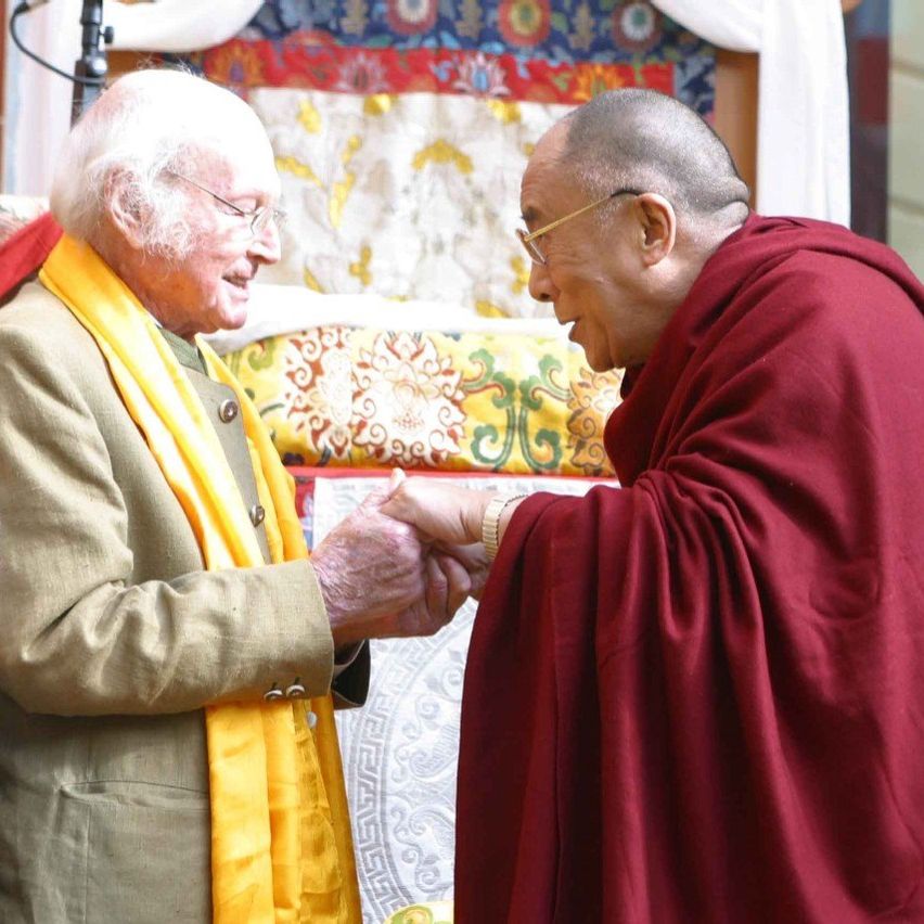 Zwei Männer, einer in einem gelben Schal und der andere in roten Roben, schütteln sich die Hände.