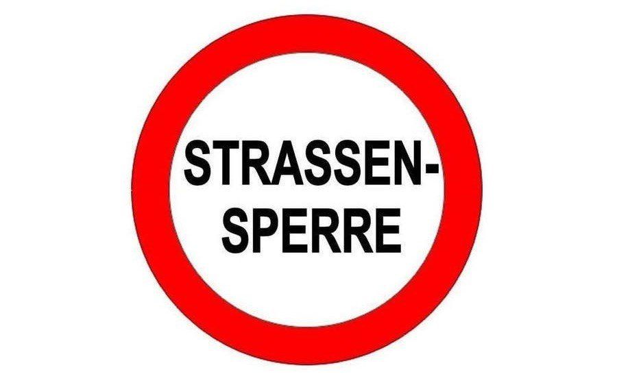 Ein roter Kreis mit weißem Hintergrund und schwarzem Text. Der Text lautet 'STRASSENSPERRE'. Es handelt sich wahrscheinlich um ein Verkehrsschild, das vor einer Straßensperrung warnt.