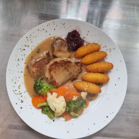 Ein Teller mit Schweinefleisch, Soße, Brokkoli, Blumenkohl, Karotten und einer Cranberry-Sauce.