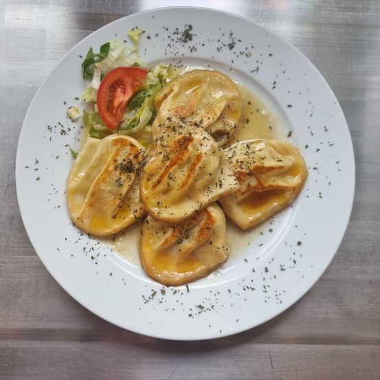 Ein Teller mit goldbraunen Knödeln mit Kräutern und einer Tomatenscheibe steht auf einer Metalloberfläche.
