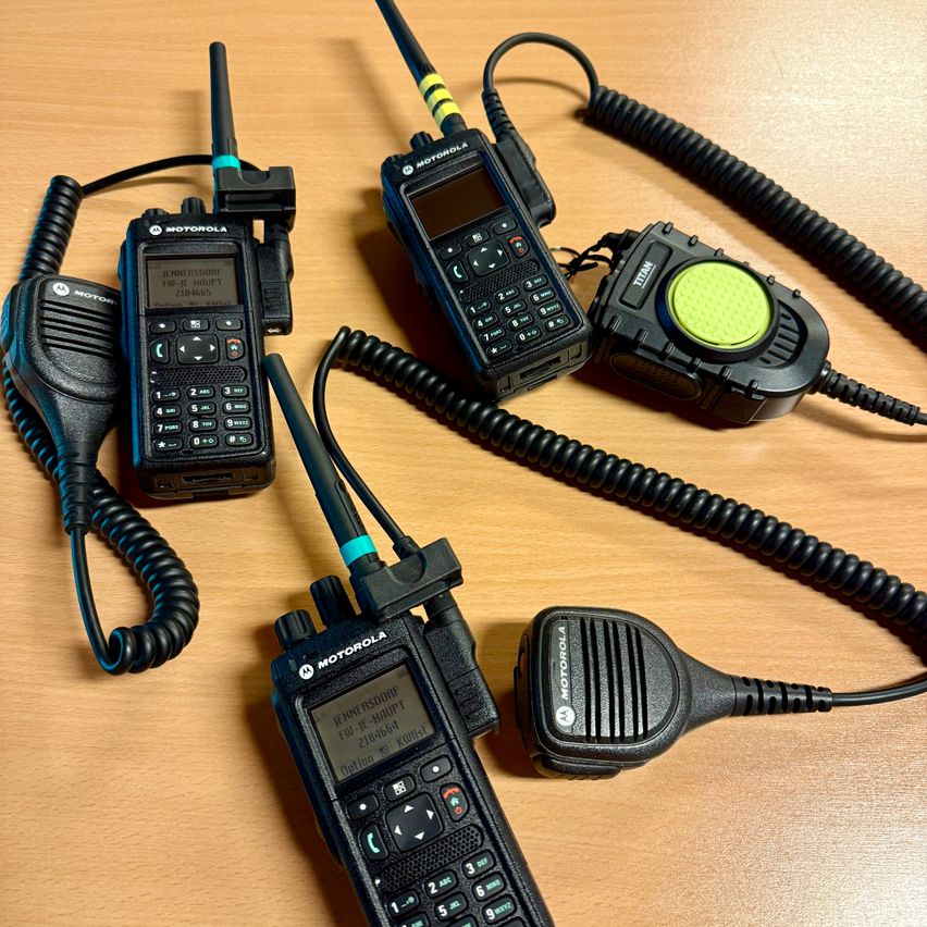 Fünf Motorola-Walkie-Talkies mit Antennen liegen auf einer Holzoberfläche. Jedes Gerät hat eine andere Größe und Anzahl von Tasten.