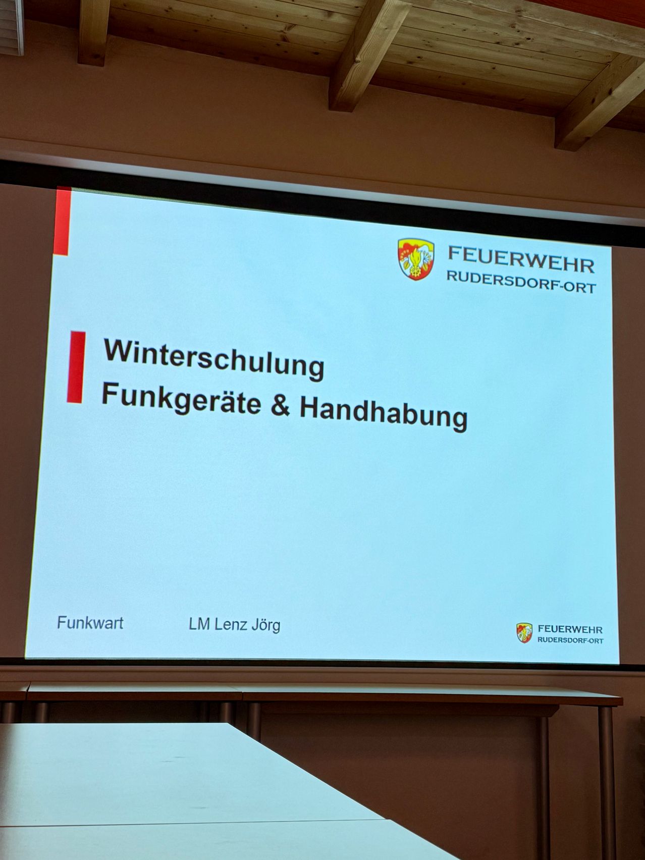 Eine Präsentationsfolie mit dem Titel 'Winterschulung Funkgeräte & Handhabung' wird angezeigt. Der Referent ist LM Lenz Jörg. Die Folie wird von Feuerwehr Rudersdorf-Ort gesponsert.
