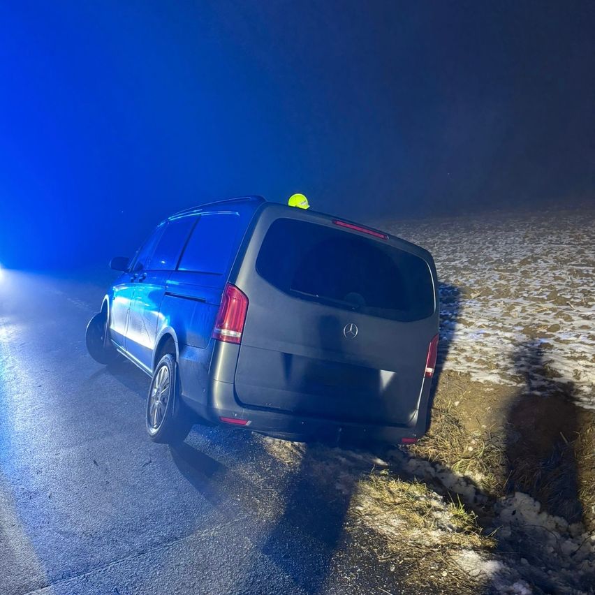 Ein dunkelblauer Mercedes-Benz-Van steht auf einer verschneiten Straße mit blinkenden blauen Lichtern. Die Rückseite des Vans ist zur Kamera gerichtet.