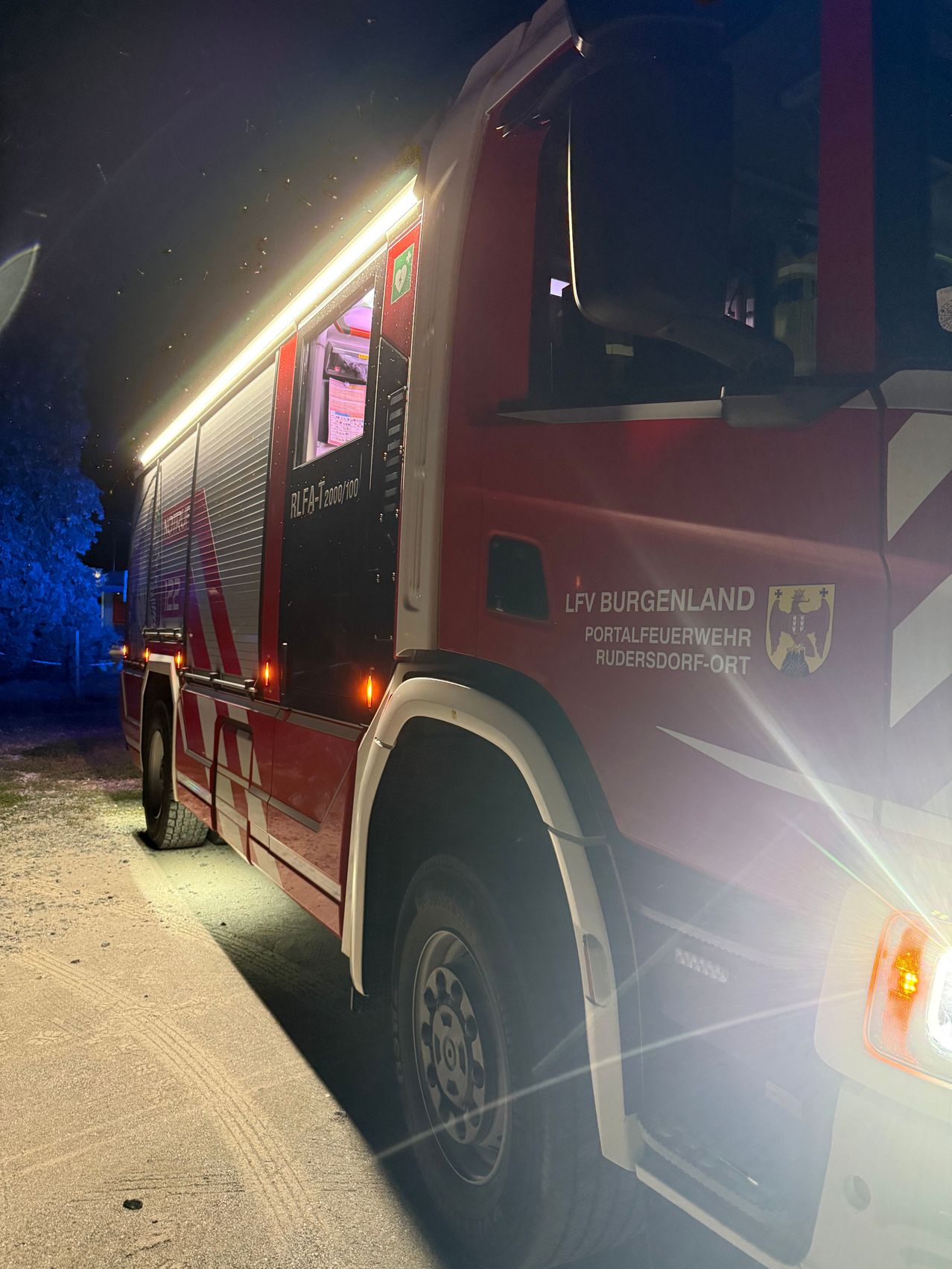 Ein roter Feuerwehrwagen mit der Aufschrift 'LFV Burgenland' und 'Portalfeuerwehr Rudersdorf-Ort' steht nachts am Straßenrand.