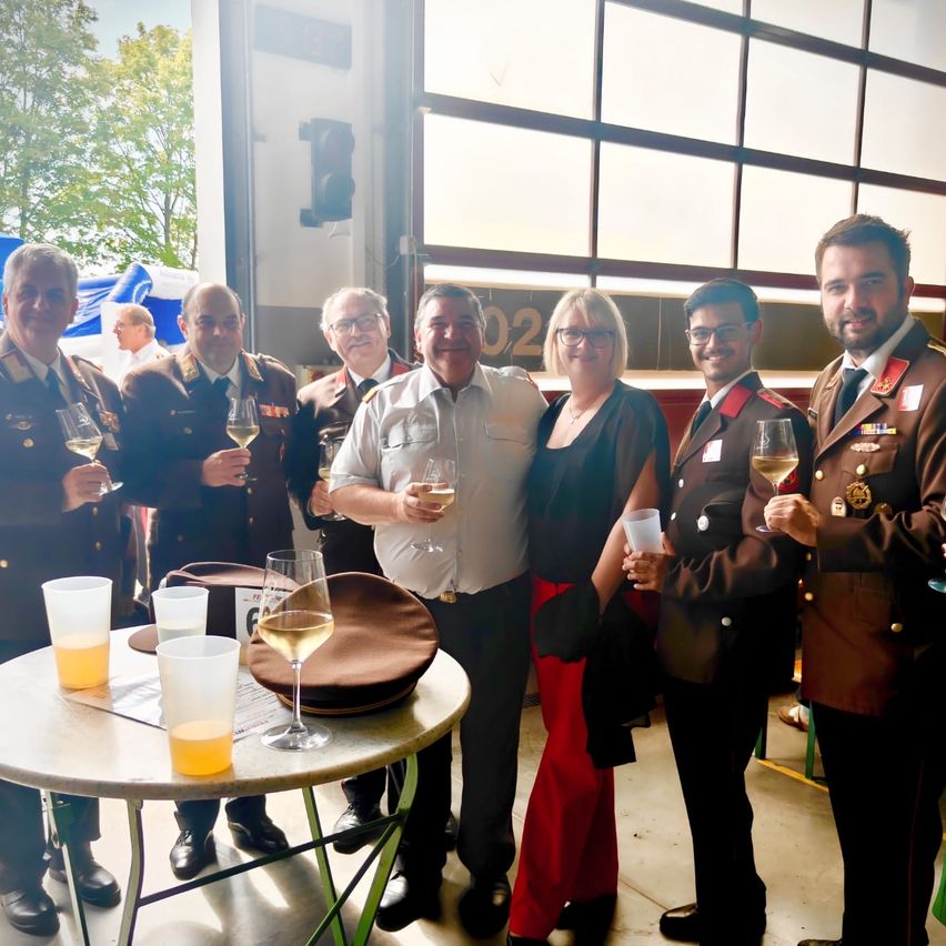 A group of military personnel and a woman are gathered around a table, holding wine glasses and smiling. They are dressed in uniforms.