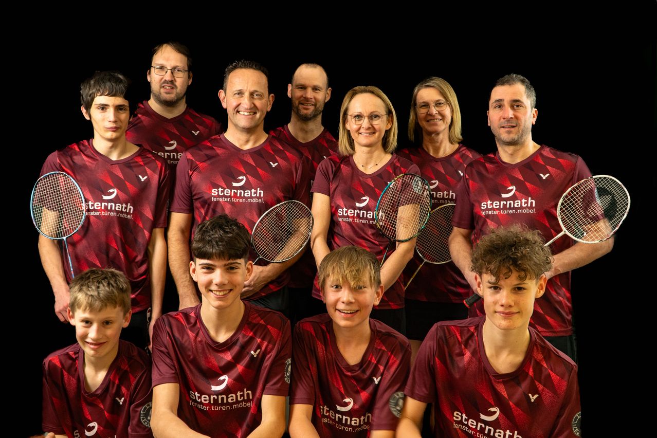 Eine Gruppe von Menschen in roten Trikots mit dem Aufdruck 'sternath', die für ein Foto posieren. Sie halten Badmintonschläger.