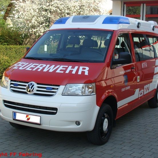 Ein roter und weißer Volkswagen-Krankenwagen ist vor einem Gebäude geparkt. Das Wort 'Feuerwehr' steht an der Seite des Fahrzeugs.