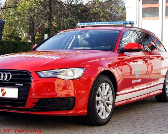 Ein roter Audi A6 Polizeiwagen, der vor einem Gebäude mit einer blauen Lichtleiste auf dem Dach geparkt ist.