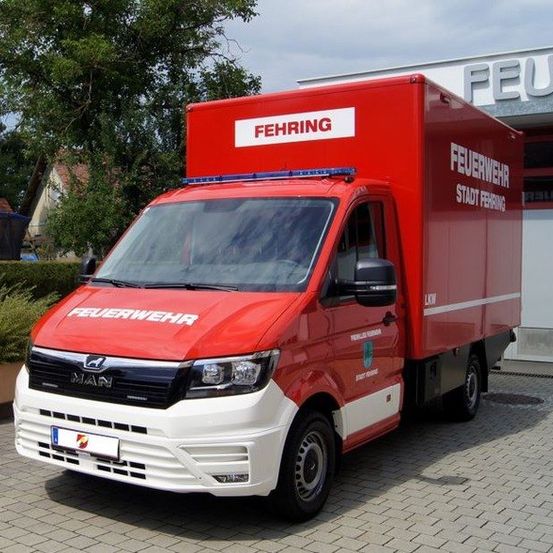 Ein roter und weißer LKW mit den Worten 'FEHRING' und 'FEUERWEHR' steht vor einem Gebäude.