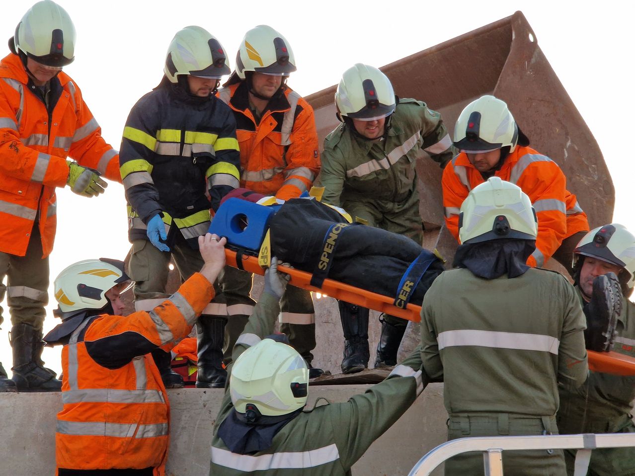 Rettungskräfte tragen eine Person auf einer Trage vor einer Baustelle. Sie tragen alle Schutzausrüstung.