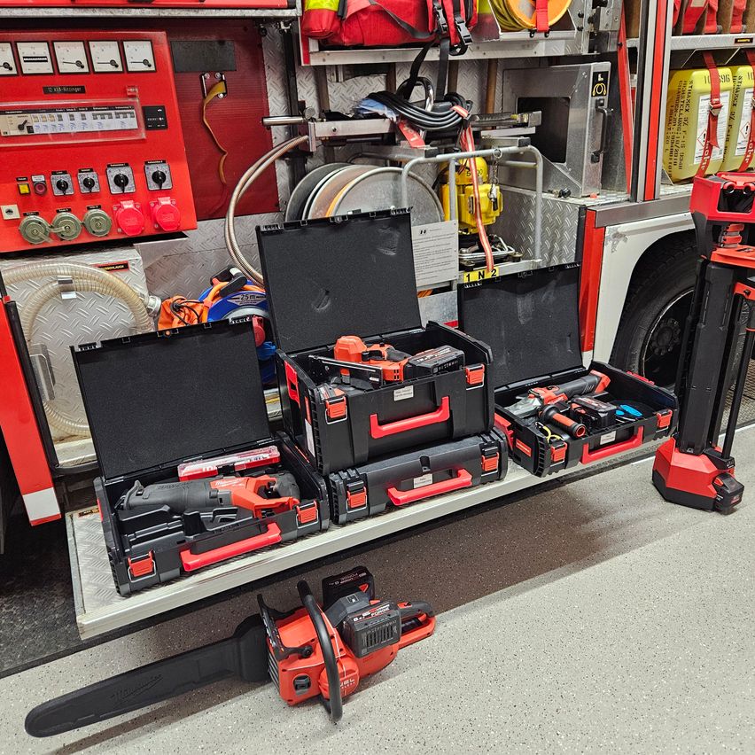 An indoor area with tools and equipment on display. Four open black and red cases with tools and one chainsaw on the floor.
