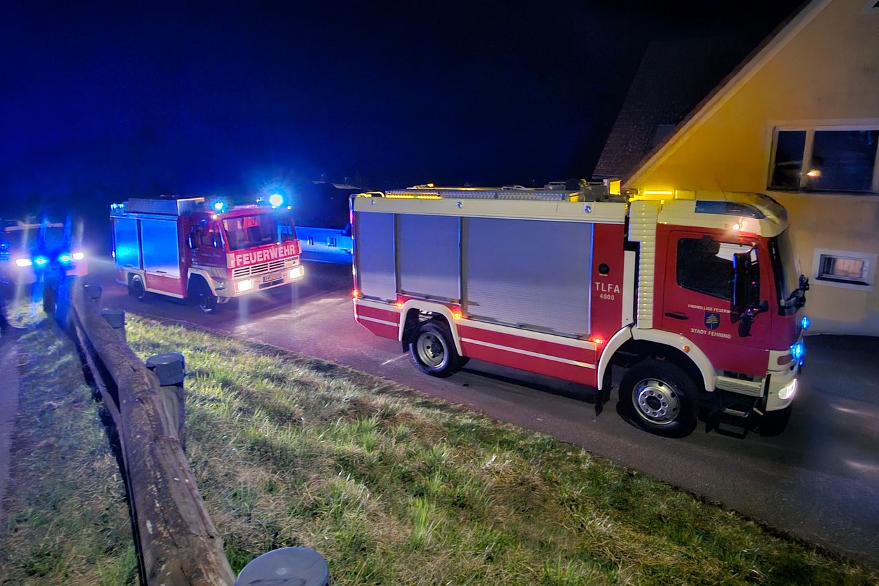Zwei Feuerwehrfahrzeuge sind nachts auf der Straße geparkt. Das vordere Fahrzeug hat seine Lichter eingeschaltet.
