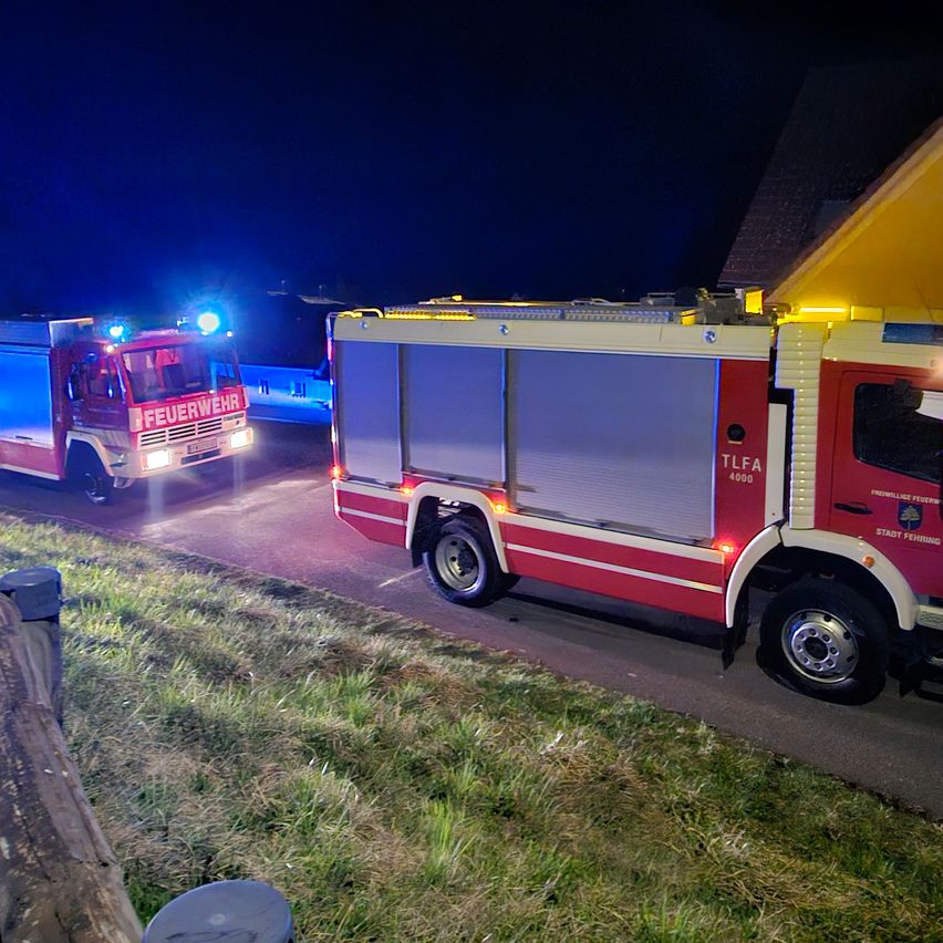Zwei Feuerwehrfahrzeuge sind nachts auf der Straße geparkt. Das vordere Fahrzeug hat seine Lichter eingeschaltet.