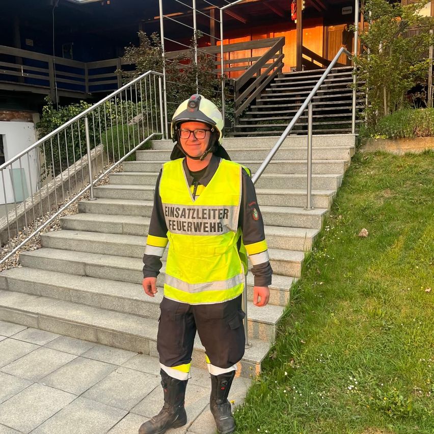 Ein Feuerwehrmann in einer reflektierenden Weste, Helm und Brille steht auf einer Betontreppe.