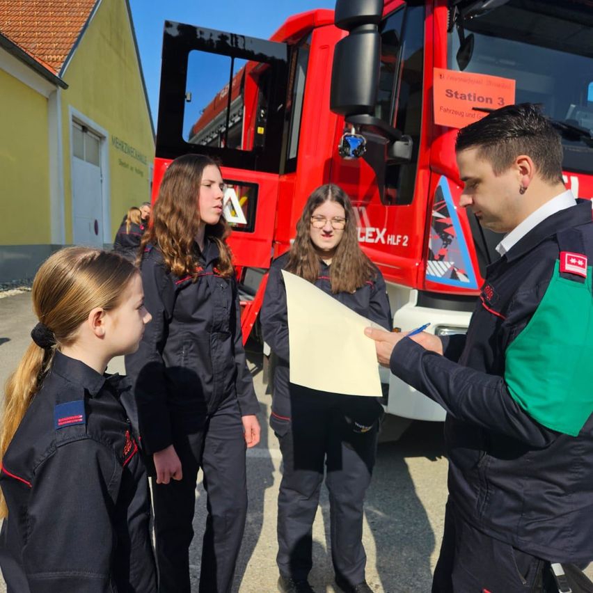 Ein Mann überreicht einer Gruppe von Frauen in Uniform vor einem roten Feuerwehrauto ein Papier.