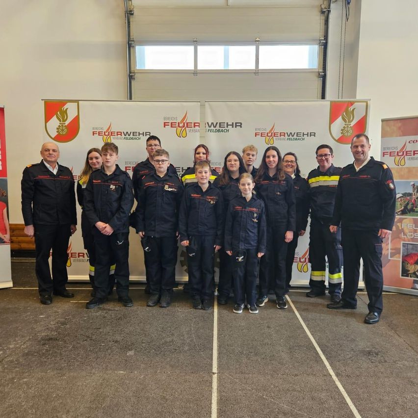 Eine Gruppe von Feuerwehrleuten und Kindern posiert vor einem weißen Banner mit Logos und Text.