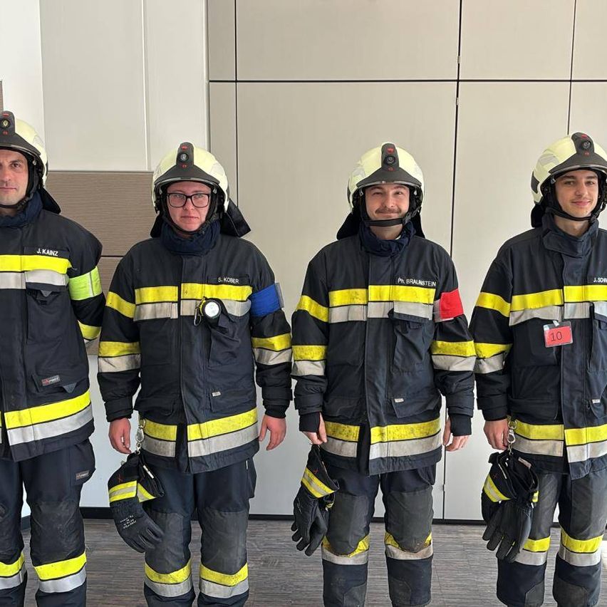 Vier Feuerwehrleute in Schutzausrüstung stehen nebeneinander mit Helmen auf. Der ganz links trägt einen Aufkleber mit der Aufschrift J. KANTZ.