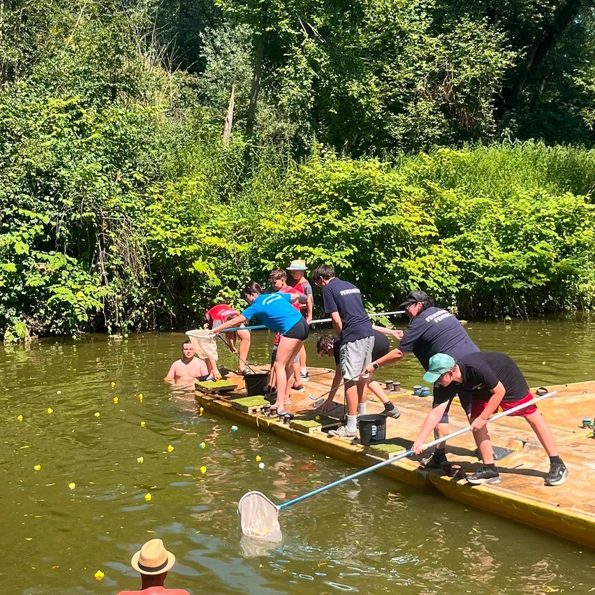 Eine Gruppe von Menschen steht auf einer schwimmenden Plattform in einem Fluss, einige sind im Wasser, und sie fangen Fische mit Netzen.