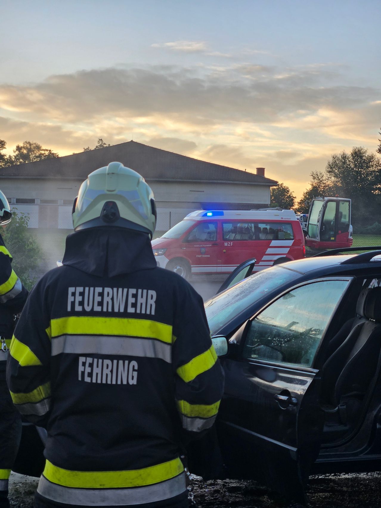 Feuerwehrleute reagieren auf einen Unfall mit einem Auto und einem Krankenwagen bei teilweise bewölktem Himmel.