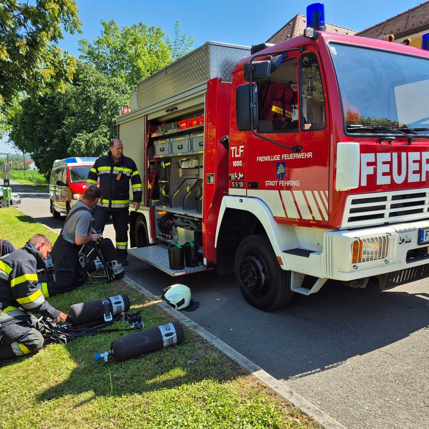 Ein Feuerwehrauto mit dem Wort Feuer ist am Straßenrand geparkt, wo drei Feuerwehrleute am Boden arbeiten.