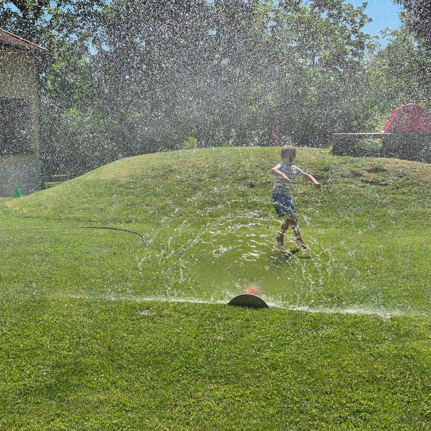 Ein Kind läuft durch einen Rasensprinkler und erzeugt einen Wasserstrahl an einem sonnigen Tag.