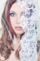 Eine Frau mit roten Haaren und blauen Augen, die eine Spitzenschleier über ihrem Gesicht trägt.