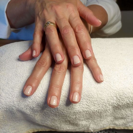 Die Hände einer Person mit lackierten Nägeln ruhen auf einem Handtuch. Die Nägel sind in einem hellen Beigeton lackiert.