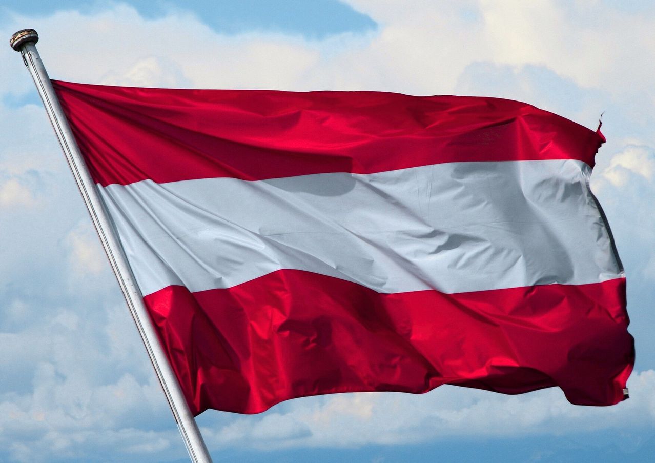 Die österreichische Flagge mit roten und weißen Streifen weht im Wind unter einem blauen Himmel mit weißen Wolken.