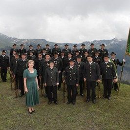 Eine Gruppe von Menschen in Uniform, die in einer Reihe mit einer Frau in der Mitte vor einer Bergkette stehen.