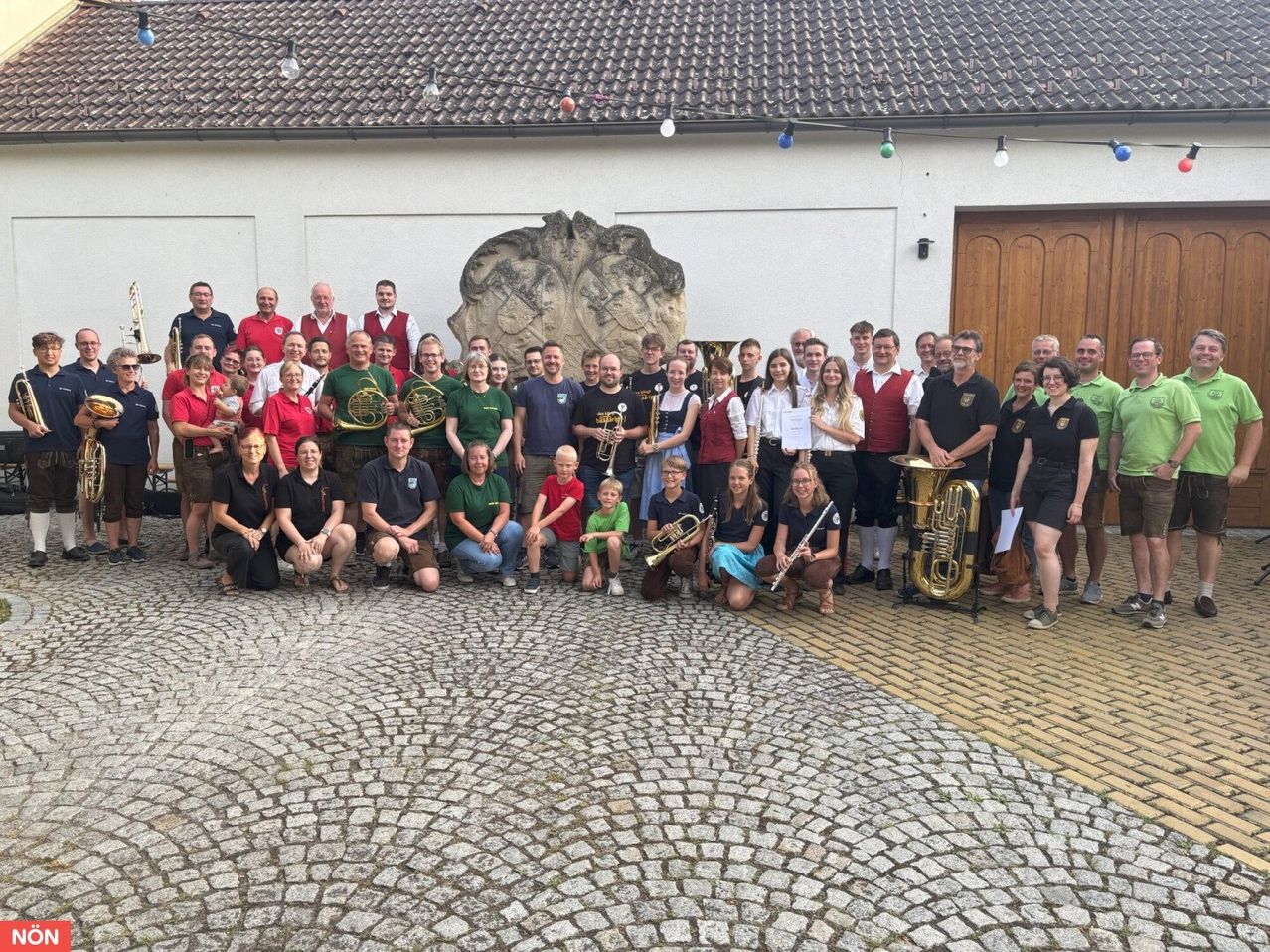 Eine Gruppe von Musikern posiert für ein Foto vor einem Gebäude. Sie halten Musikinstrumente in den Händen. Einige von ihnen tragen traditionelle Kleidung.