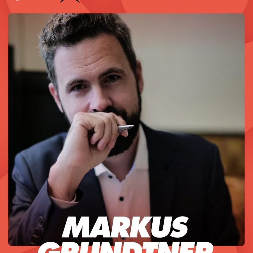 Ein Mann in einem Anzug, identifiziert als Markus Grundtner, hält einen Stift in der Hand und sieht nachdenklich aus.