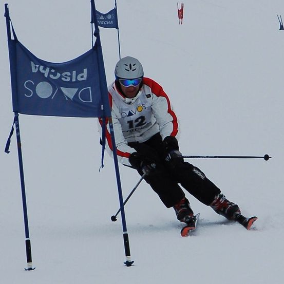 Ein Skifahrer mit Helm und Brille navigiert durch einen Parcours und hält Skistöcke. Der Parcours ist durch Flaggen gekennzeichnet, darunter eine mit der Aufschrift Davos.
