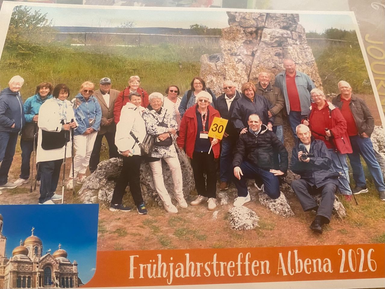 Eine Gruppe von Menschen posiert für ein Foto vor einer Felsformation. Sie tragen alle Winterkleidung. Ein Mann sitzt auf einem Felsen und hält eine Kamera.