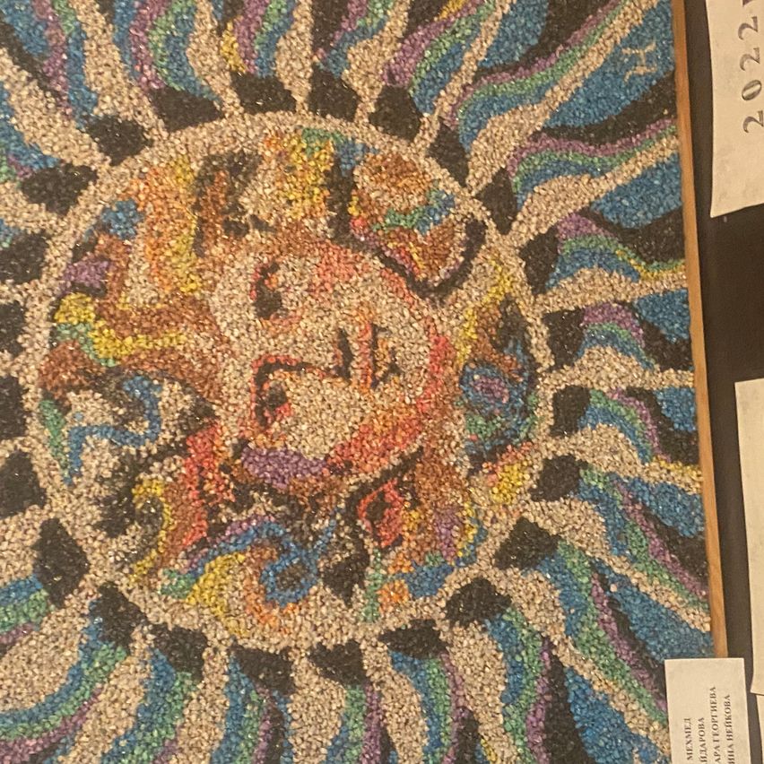 Ein farbenfrohes, mosaikartiger Kunstwerk mit einem zentralen Sonnendesign, umgeben von wirbelnden Mustern. Dargestellt auf schwarzem Hintergrund mit Etiketten an den Seiten.