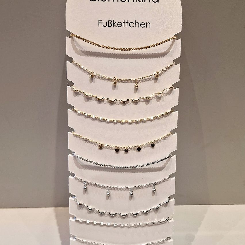 Eine Ausstellung mehrerer Halsketten mit verschiedenen Designs, vertikal auf einem weißen Ständer angeordnet. Die Halsketten sind aus Gold und Silber mit verschiedenen Anhängern.