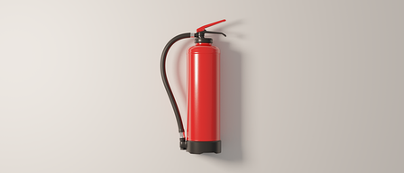 Ein roter Feuerlöscher mit schwarzem Schlauch ist an einer hellgrauen Wand montiert.