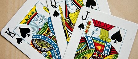 Three playing cards are displayed on a wooden surface: the King of Spades, the Queen of Spades, and the Jack of Spades.