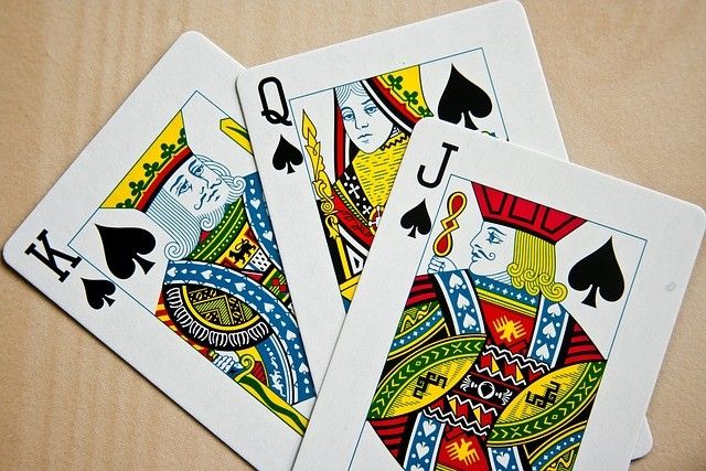 Drei Spielkarten sind auf einer Holzoberfläche zu sehen: der Pik-König, die Pik-Dame und der Pik-Bube.