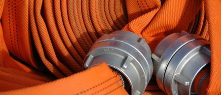 Eine Nahaufnahme eines orangefarbenen Feuerwehrschlauchs mit metallischen Anschlüssen, die die Textur und die Nähte des Gewebes zeigt.