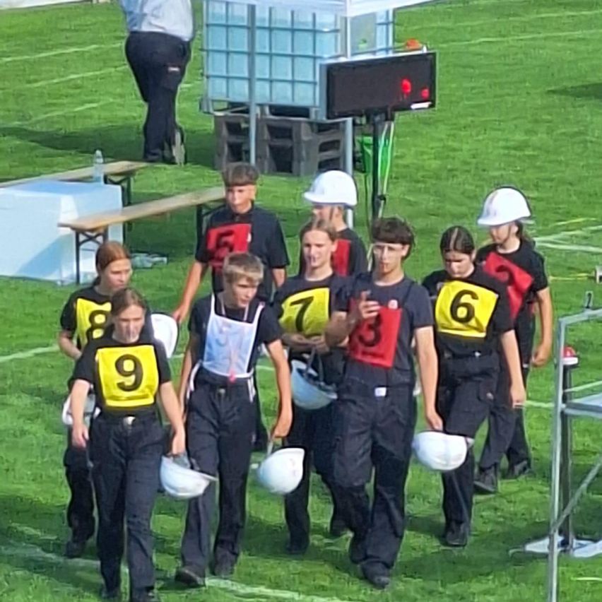 A group of young people wearing numbered shirts and white helmets are walking on a field.