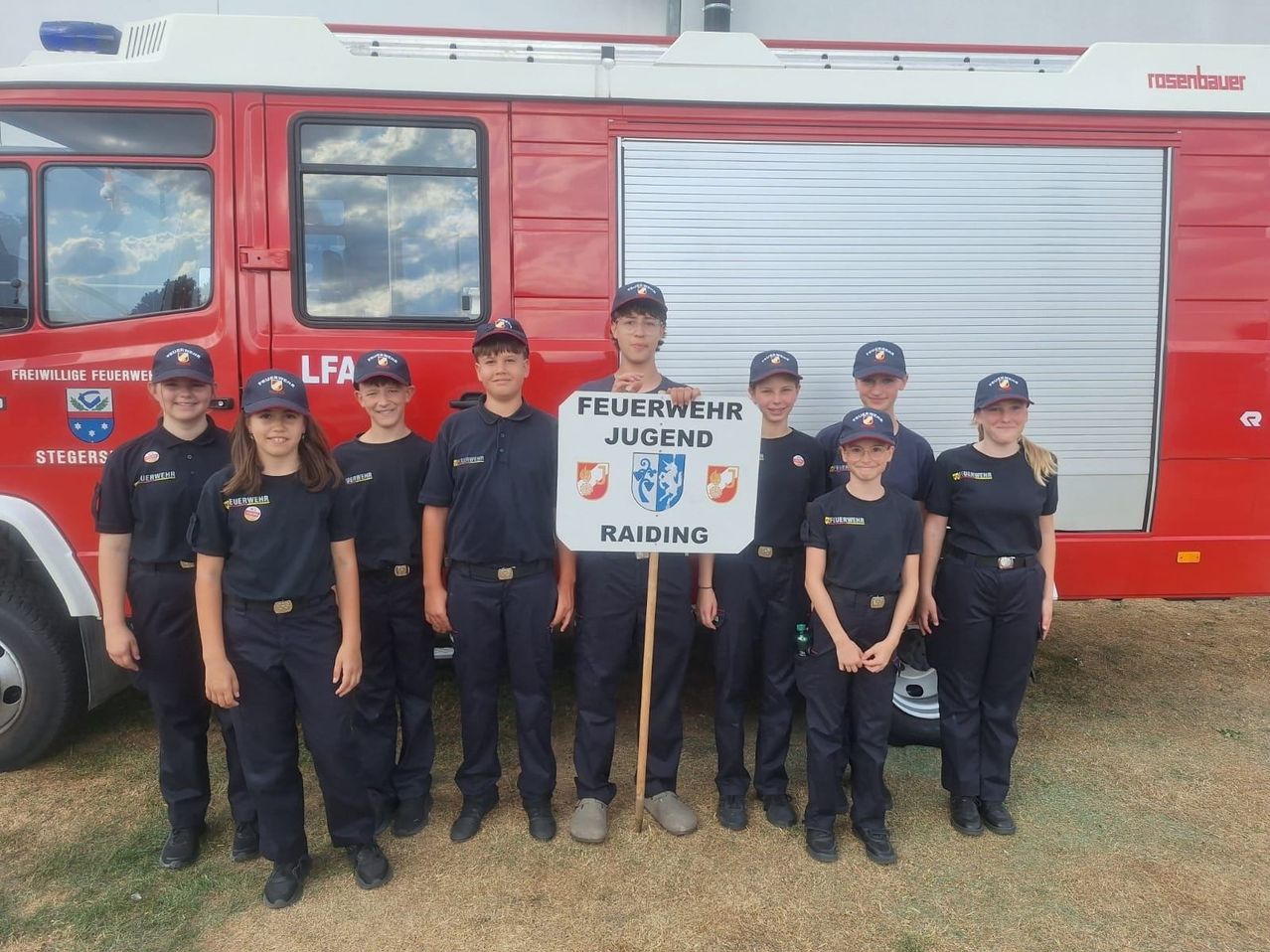 A group of young firefighters in uniform pose for a photo in front of a fire truck.