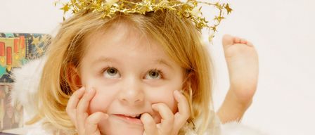 A young girl in a white angel costume with a gold crown of stars smiles for the camera.