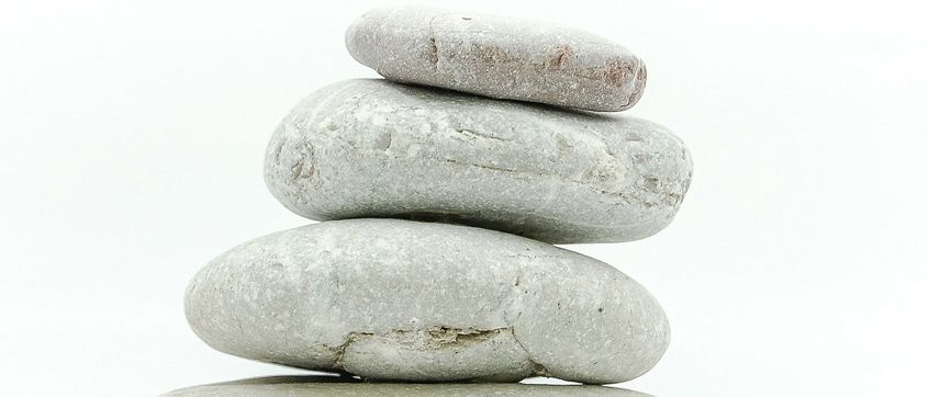 Fünf graue Steine sind auf einem weißen Hintergrund vertikal gestapelt. Jeder Stein hat eine einzigartige Textur. Der oberste Stein ist größer und hat einen rötlichen Fleck.