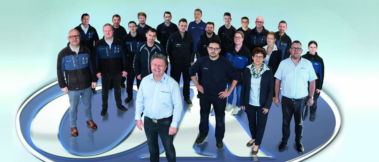 Eine Gruppe von Menschen, die in Blau und Schwarz gekleidet sind, steht vor einem blau-weißen Logo. Sie lächeln und scheinen für ein Foto zu posieren.